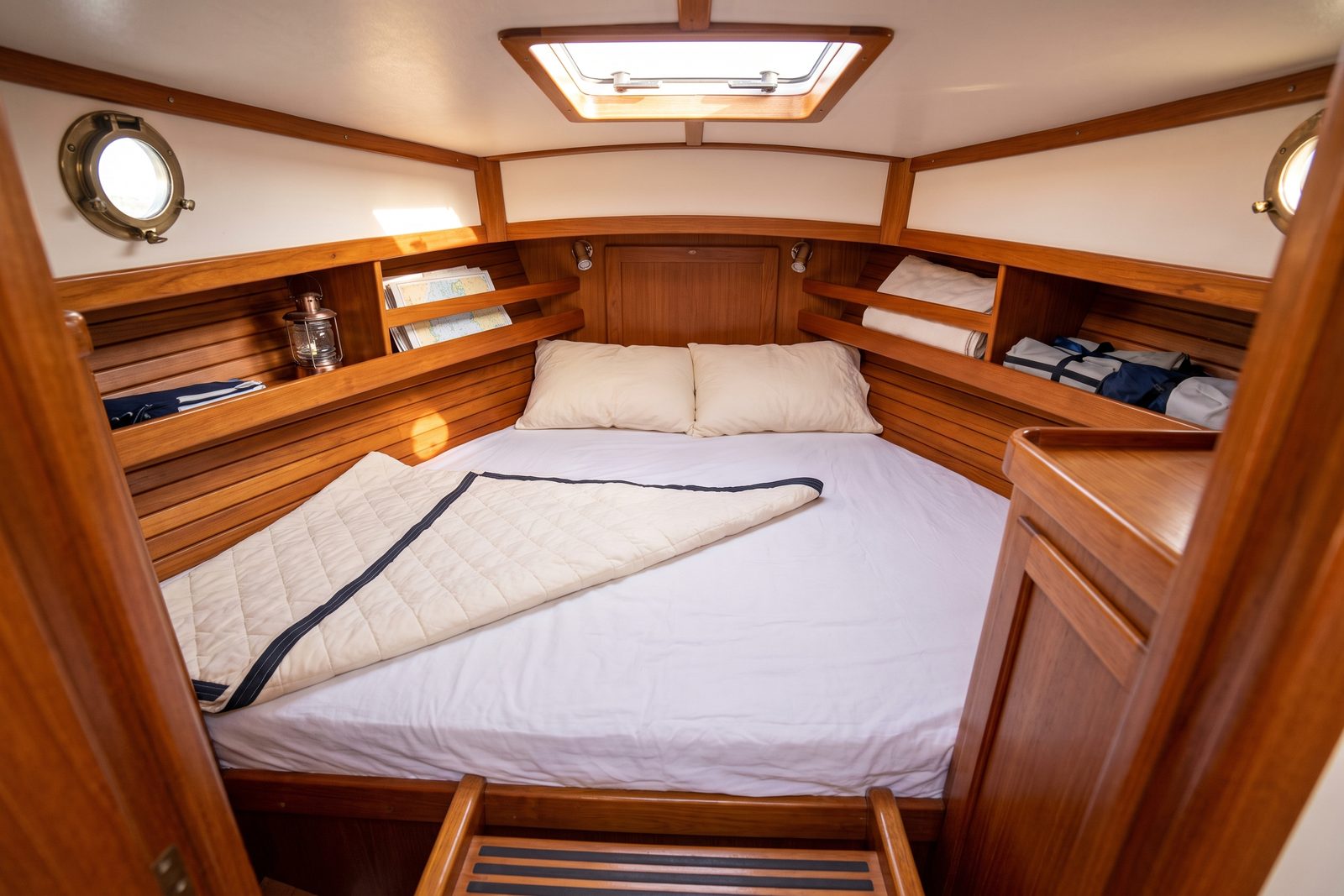 Custom V-berth mattress cut to fit the tapering bow cabin of a boat, made up with white linen